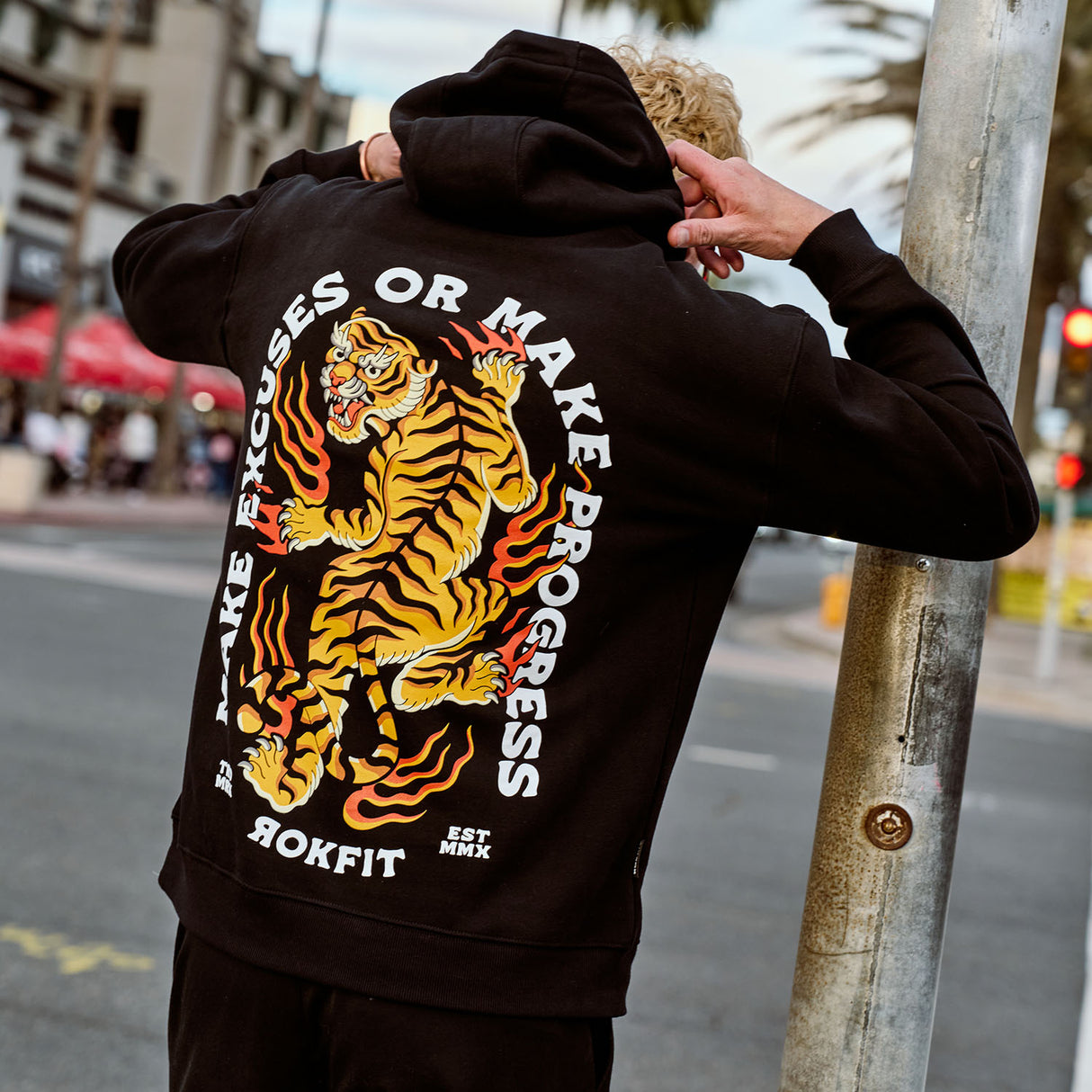 Male model outdoors wearing hoody with 'Make Excuses or Make Progress' graphic