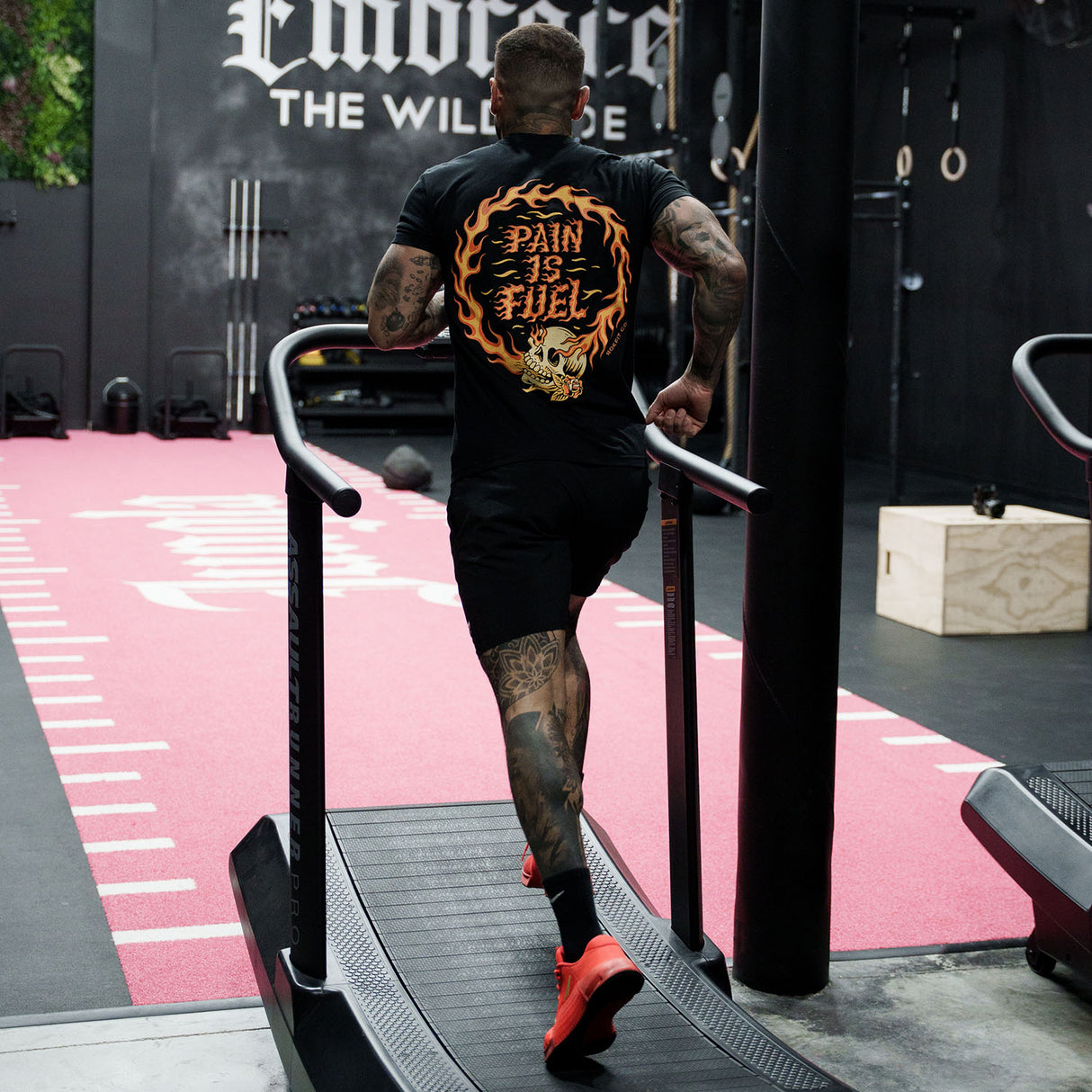 Male model running in a gym wearing Active Tee with 'Pain Is Fuel' graphic