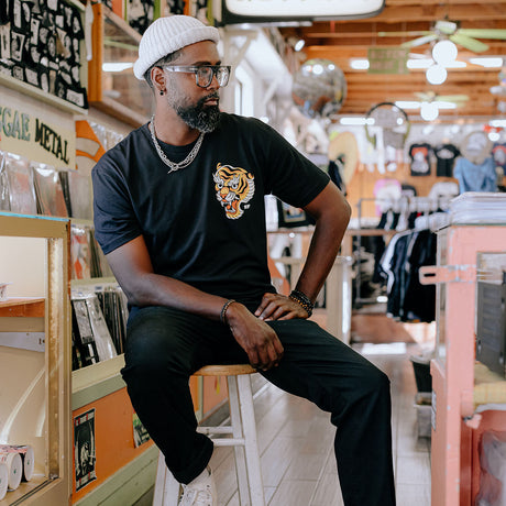 Male model in record store wearing unisex Active Tee with 'Make Excuses or Make Progress' graphic