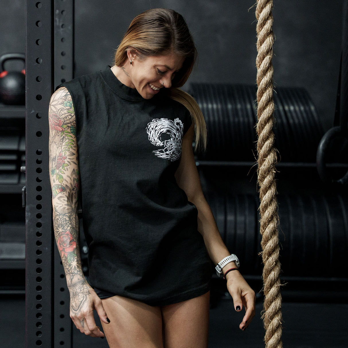 Female model in a gym wearing sleeveless Street Tee with 'Own The Grind' graphic